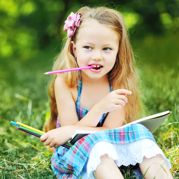 Чарівна маленька дівчинка з олівцями і нотою в парку — стокове фото