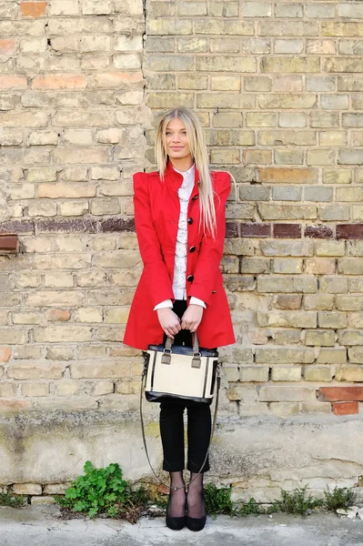 Chica de moda en vestido rojo con bolsa de pie cerca de una pared —  Fotos de Stock