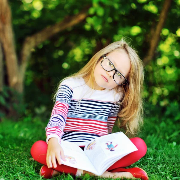 Sad little girl with a book in a park — Stock Photo, Image