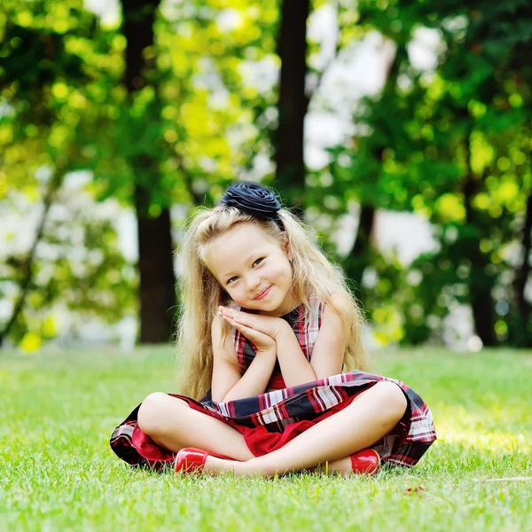 Egy mosolygó kislány portréja, aki zöld füvön ül. — Stock Fotó