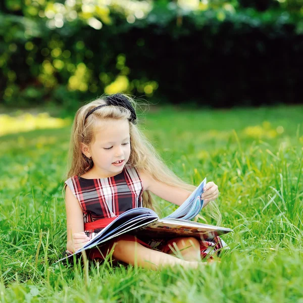 Ευτυχισμένο κοριτσάκι που διαβάζει ένα βιβλίο στο πάρκο. — Φωτογραφία Αρχείου