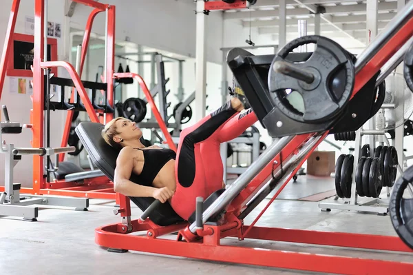 Ajuste piernas de entrenamiento de mujer en un simulador de pierna en el gimnasio — Foto de Stock