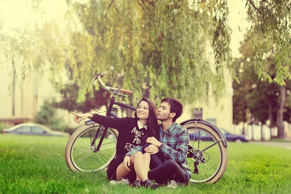 Jovem casal bonito sentado perto de uma bicicleta vintage e apontando Fotos De Bancos De Imagens Sem Royalties