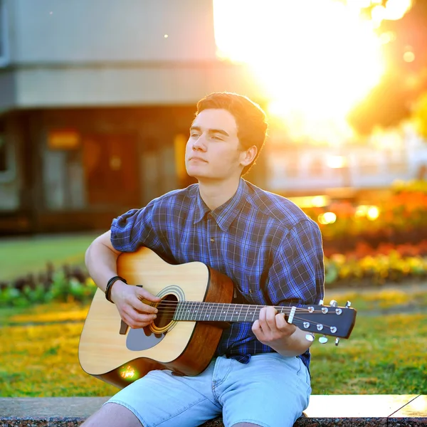 Mladý muž, hraje na akustickou kytaru v letním parku — Stock fotografie