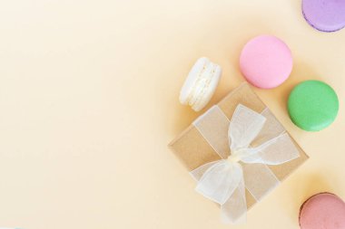 Kurdeleli ve renkli badem kurabiyeli mevcut kutu, bej arkaplanlı badem kurabiyeleri. Kutlama, doğum günü etkinliği. Düz konum, üst görünüm, kopyalama alanı.