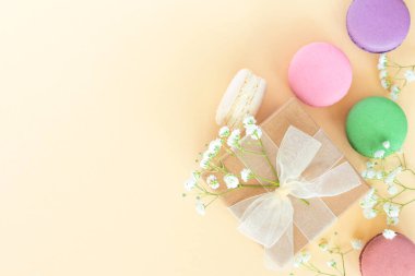 Kurdeleli ve renkli badem kurabiyeli mevcut kutu, bej arkaplanlı badem kurabiyeleri. Kutlama, doğum günü etkinliği. Düz konum, üst görünüm, kopyalama alanı.