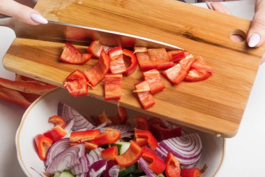 Kesme tahtasındaki dilimlenmiş kırmızı biber bir salata kasesine aktarılır..