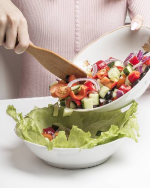 Bir kadın yeşil marul yapraklı bir kaseye Yunan salatası koyar..