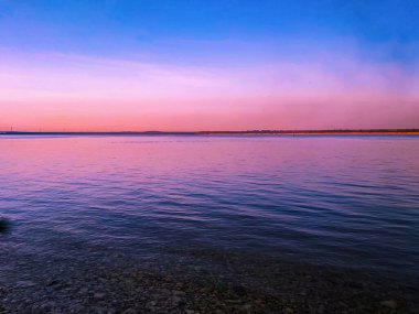 Geniş mavi bir nehrin üzerinde kıpkırmızı bir gün batımı.
