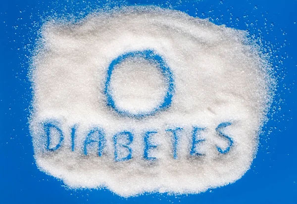 Şeker hastalığı ve şeker hastalığının sembolü mavi arka plandaki şeker kumunun üzerine yazılmıştır..