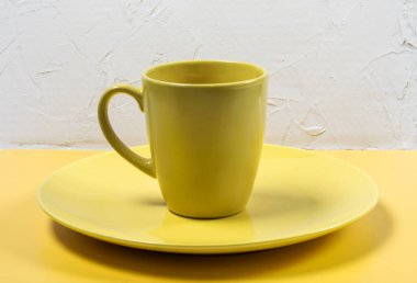 Sarı ve beyaz desenli arka planda boş bir sarı tabak ve fincan..