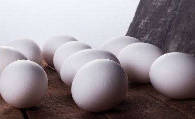 Beyaz arka planda, ahşap bir masanın üzerinde bir sürü beyaz yumurta..