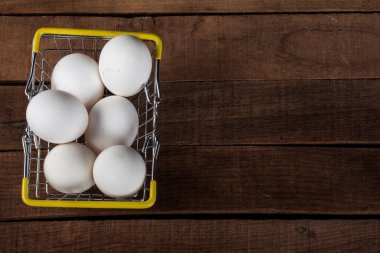 Demir bir yemek sepetinde beyaz yumurtalar, ahşap bir masanın üstünde, üst manzara, uzayın bir kopyasıyla..