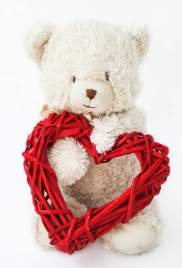 Beyaz bir arka planda patilerinde örgülü kırmızı bir kalbi olan beyaz bir oyuncak ayı..