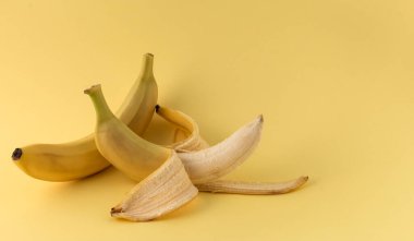 Biri soyulmuş, biri soyulmamış sarı muz ve sarı arka planda, boşluğun bir kopyası var..