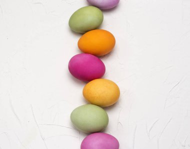 Parlak Paskalya yumurtaları beyaz dokulu arka planda düz bir sıra halinde uzayın bir kopyasıyla yatıyordu..