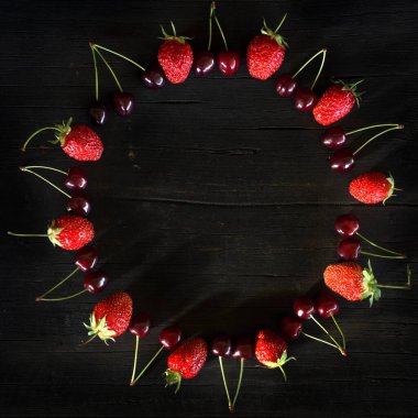 Siyah ahşap arka planda çilek ve kiraz. Düz konum, üst görünüm boşluğun bir kopyasıyla.