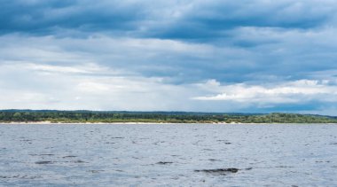 Fırtınalı bir nehrin üzerinde yeşil kıyıları olan bulutlu bir gökyüzü.