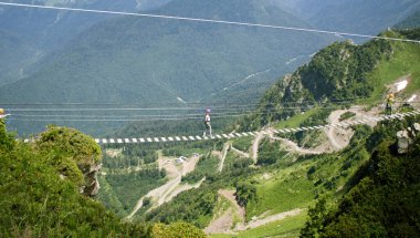 Kafkasya dağlarında bir uçurumun tepesindeki ip köprüde aşırı yürüyen insanlar..