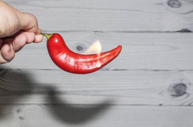 Elimde, beyaz ahşap bir arka planda alevdeki acı kırmızı biber..