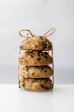 Yuvarlak yulaf ezmesi ya da çikolata parçalı kurabiyeler beyaz arka planda yansıtıcı yüzeyde bir iple bağlanmış.