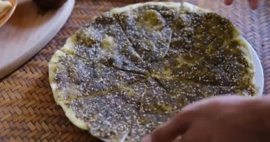 Zaatar Manakish 'i kesen bir ele yaklaş. Zeytinyağı ve zaatar ile kaplanmış yassı ekmek. Geleneksel Arap yemekleri.
