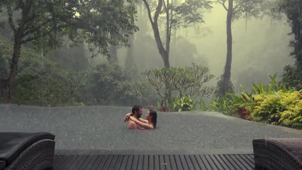Belo jovem casal desfrutando juntos na piscina infiniti com vista para a floresta nebulosa tropical durante a chuva — Vídeo de Stock
