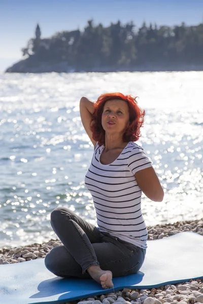 Woman performing joga on sea coast, on windy sunny day — Stock Photo, Image