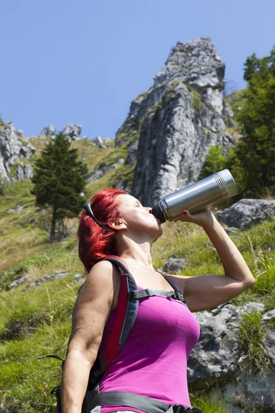 Donna escursionista bere mentre riposa in alto in montagna — Foto Stock