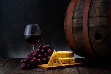 Eski ahşap masada bir bardak kırmızı şarap, peynir ve üzüm. koyu arkaplan.