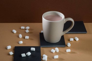 Bir parça acı çikolata, kakao tozlu kaşık ve kahverengi bir masada bir bardak kakao..