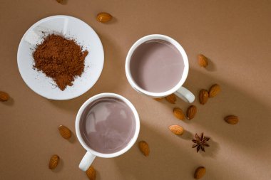 Sıcak içeceklerle dolu iki kupa bir tabak kakao tozu ve bademlerin yanında bir masada oturuyor. Bazı baharatlar etrafa saçılmış. Bu sahne dinlendirici bir öğleden sonra sergiliyor.