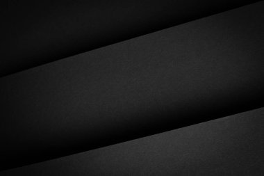 Sahne, farklı çizgiler ve gölgeler oluşturan katmanlı karanlık bir yüzeyi gösteriyor. Doku minimalist bir yaklaşımla pürüzsüz görünüyor. Odaklanma şekli ve kontrasttır.