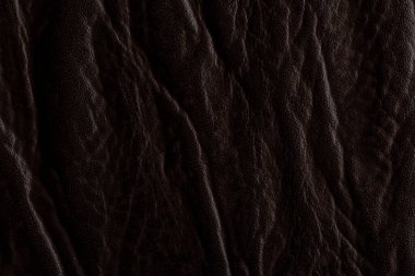 Yüzeyindeki kırışıklıkları ve kıvrımları gösteren koyu deri görüntüler. Doku yumuşak ve zengin görünüyor, materyalin detaylarını vurguluyor. Işık deseni ve derinliği arttırır.