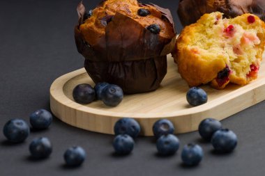 Taze pişmiş kekler dağınık yabanmersinleriyle çevrili ahşap bir tabakta otururlar. Sahne yemek malzemelerine odaklanmış rahat bir mutfağı gösteriyor..