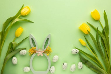Renkli bahar sergisi çiçek desenli tavşan kulakları, etrafa dizilmiş sarı laleler ve yeşil bir yüzeye dağılmış benekli yumurtalar gösteriyor. Bu kurulum Paskalya şenliklerini karşılıyor.