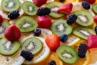 Parlak renkler tabağı taze meyvelerle doldurur. Kivi, limon ve portakal dilimleri çilek, böğürtlen ve böğürtlen ile düzenlenir..