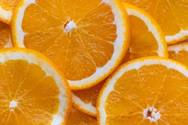 Turuncu dilimler düz bir yüzeyde parlak renklerle düzenlenir. Yuvarlak dilimler sulu meyvenin dokusunu ve iç yapısını gösteriyor. Güneş ışığı taze görünüşlerine vurgu yapar.