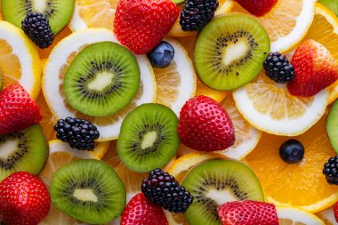 Portakal, limon, kivi ve böğürtlen dilimleri düz bir yüzeye yayılır. Meyvelerin parlak renkleri canlı bir sahne yaratır. Bu düzenleme çeşitli doku ve tatları gösterir.