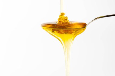 Bal, kaşıktan akarak altın çağlayanı oluşturur. Parlak renk, sunum için alan sağlayan düz beyaz arkaplanla çelişiyor.