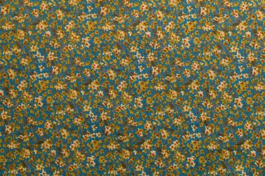 Kumaş mavi arka planda çeşitli renklerde küçük çiçek desenleri gösteriyor. Tasarım birbirine yakın, tekstil kullanımı için zengin bir görsel doku oluşturuyor..