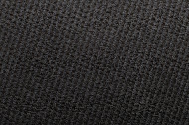 Resim, görünür dokusu ve deseni olan koyu renkli bir kumaşın yakın görüntüsünü gösteriyor. Kumaş kapalı bir ortamda ve gündüz saatlerinde doğal ışıkla aydınlatılıyor..