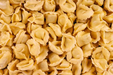 Ham sarı tortellini makarnasının tam kare kompozisyonu. Taze ve pişmemiş, bu İtalyan gıda arka planı, aşçılık tasarımı ve reklamı için ideal doku ve şekli ön plana çıkarıyor..