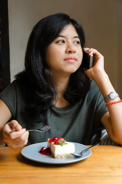 Young woman talking mobile phone with a cake in cafe — Stock Photo, Image