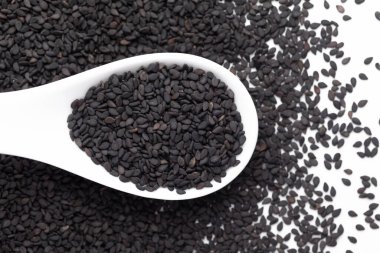 Macro Black Susam Tohumları (Sesamum indicum) ya da beyaz seramik çorba kaşığı kabuklu Black Til. Üst görünüm, kendi gradyan arkaplanı üzerinde.