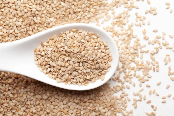 Organik Beyaz Susam tohumları (Sesamum indicum) ya da beyaz seramik çorba kaşığında kabuklu beyaz Til. Üst görünüm, kendi gradyan arkaplanı üzerinde.