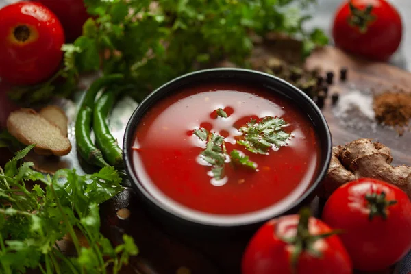 Close-up of Indian Homemade fresh and healthy tomato soup garnished with fresh coriander leaves and ingredients and herbs, served in a black bowl over the wooden top background.