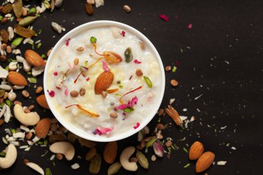 Safran ve kuru meyvelerle süslenmiş kremalı pirinç kheer (khir) yakın çekim. Hint usulü lezzetli tatlı. Beyaz seramik kasede servis ediliyor. Siyah arkaplanda Üst Görünüm.