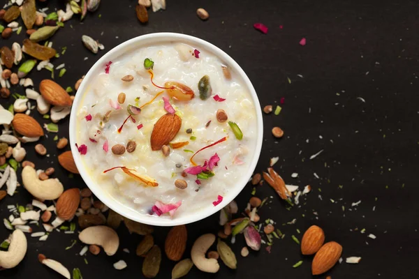 Safran ve kuru meyvelerle süslenmiş kremalı pirinç kheer (khir) yakın çekim. Hint usulü lezzetli tatlı. Beyaz seramik kasede servis ediliyor. Siyah arkaplanda Üst Görünüm.