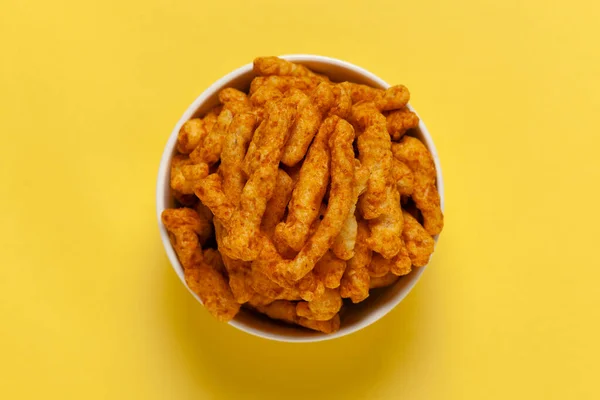 Close up of tangy Potato Puff Snacks sticks, Popular Ready to eat crunchy and puffed snacks sticks tangy spicy  orange color over yellow background